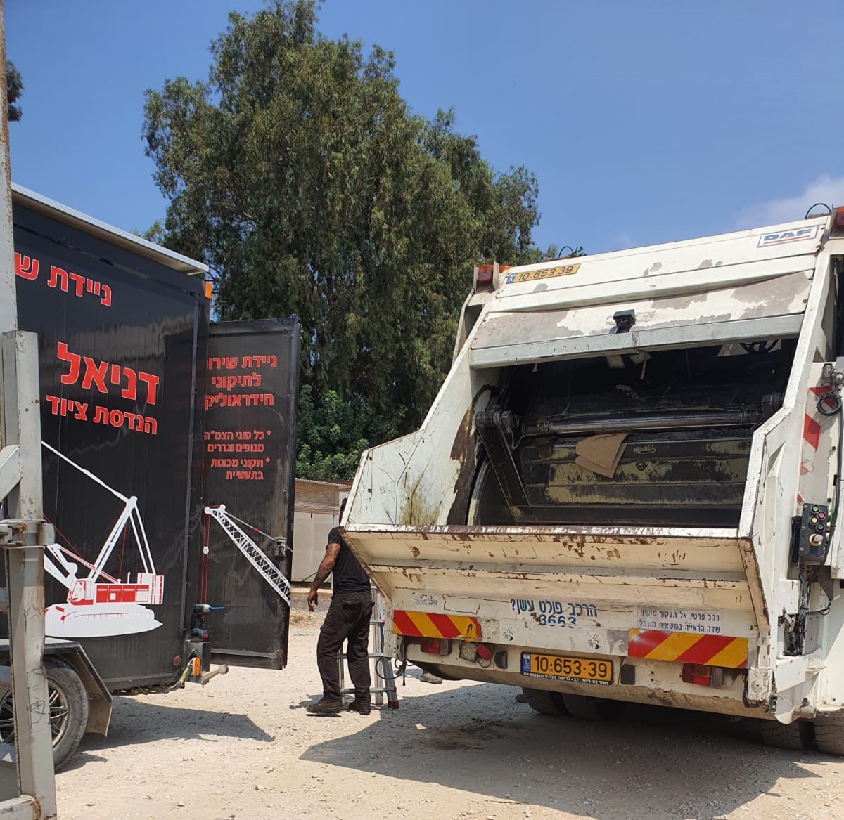 טכנאי מתקן דחסן אשפה ליד ניידת השירות